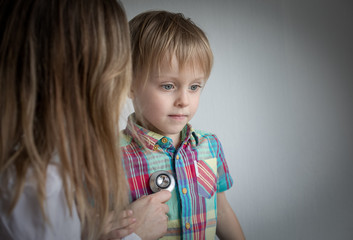 Naklejka premium little boy at the doctor, female using stethoscope.