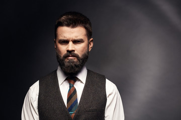 Studio portrait of angry and serious attractive man with dark hair and mustache in white shirt, brown vest, colorful tie. Old fashioned style, gentleman.