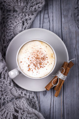 Coffee cappuccino with cinnamon and knitted scarf on a gray background