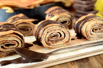 Crepes rolls with chocolate sauce on a wooden board