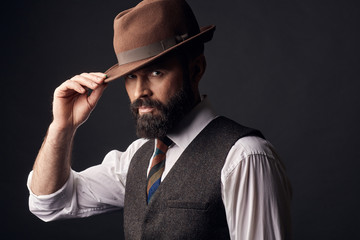 Studio portrait of handsome man with dark hair, mustache and beard in white shirt, brown vest,...