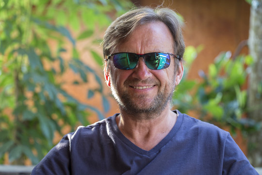 Portrait of an unshaven middle-aged man in sunglasses relaxing on the nature in summer day