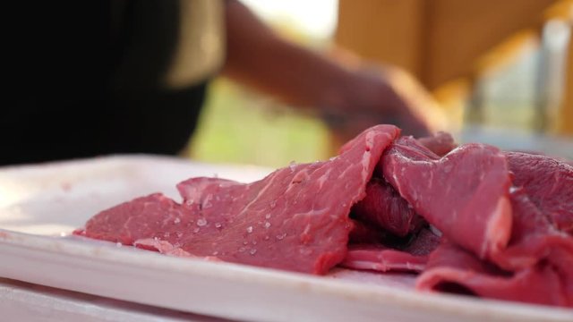 Man cooks raw meat and vegetables on a barbeque grill in summer