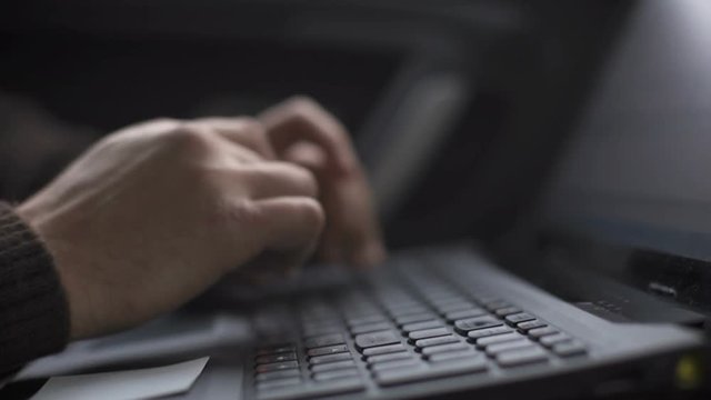 A man is working in a car typing text on a laptop