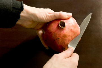 Close-up of hands cutting open a pomegranate with a stainless steel knife - dark background