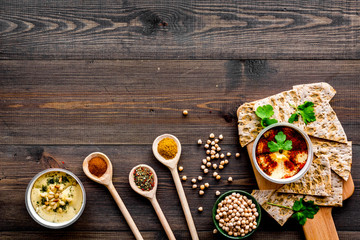 Serve hummus. Bowl with dish near pieces of crispbread on dark wooden background top view copy space