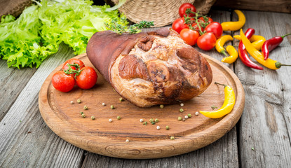 Smoked ham hock with herbs and spices on wooden plate.
