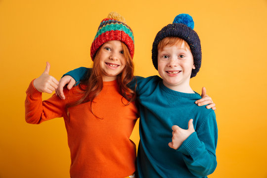 Funny little children wearing warm hats showing thumbs up.
