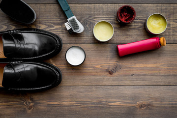 Shoe polish, brushes, wax near black shiny leather shoes on dark wooden background top view copy space
