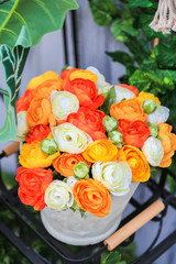 A colorful artificial flowers in a white pot on black metal shelf with nature background.