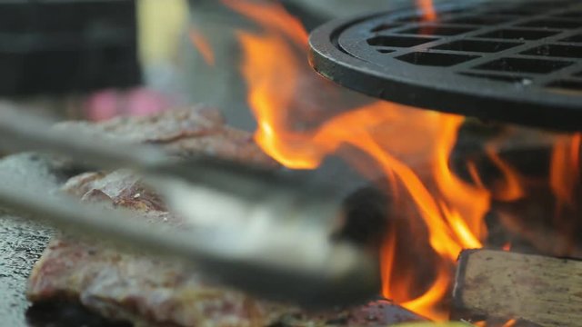 Cook turns pieces of meat on the grill with tongs. Meat roasted on fire with rosemary