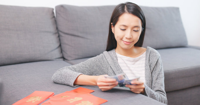 Woman putting money banknote into red packet at home