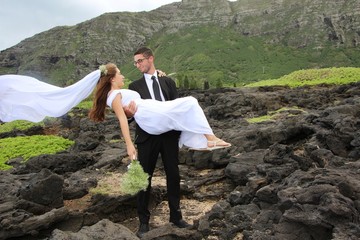 the groom is taking his bride in his arms. It's on a mountain in Hawaii