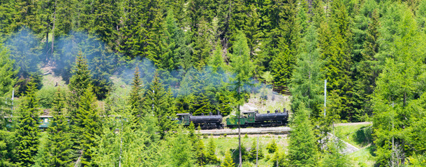 Steam train. Historical retro steam train in the mountains of the Alps. Smoke from the pipe.