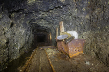 Underground abandoned ore mine shaft tunnel gallery with ore cart and sleeping miner