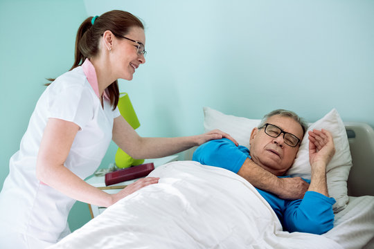 Nice smiling nurse looking at patient who sleeping and dreaming
