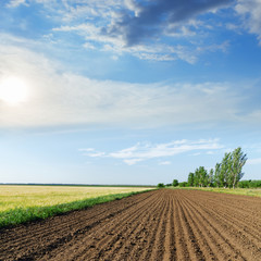 black agriculture field and sun in blue sky with clouds