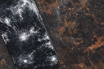 Modern smartphone with large broken screen with debris on the grunge backgdound with copy space