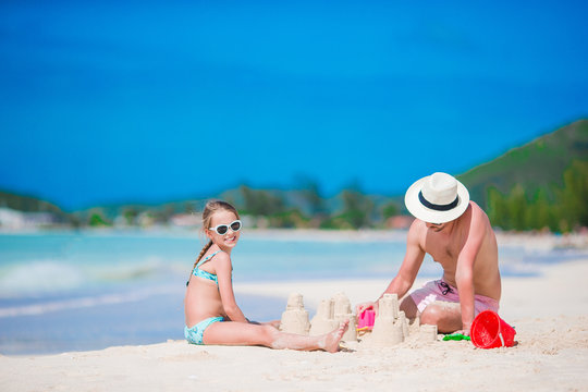 Family making sand castle at tropical white beach. Father and girl playing with sand on tropical beach