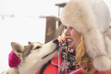 Fototapeta premium Young woman in winter clothes, smiling broadly and hugging a dog with blue eyes Husky