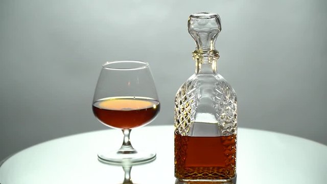A glass and a decanter with cognac slowly rotate on a mirror table