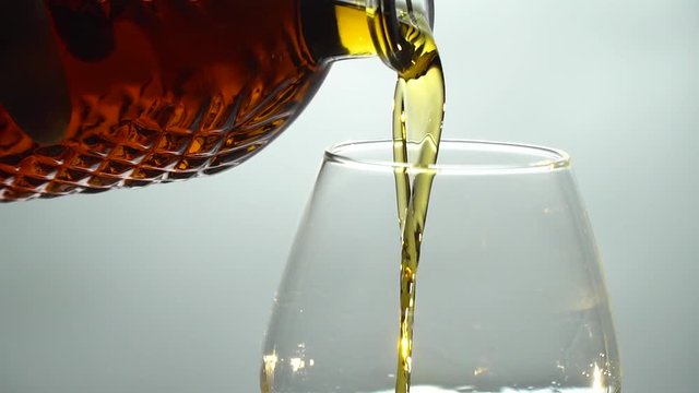 The hand pours cognac into the glass from the crystal decanter, slow motion