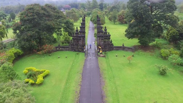 Away gliding aerial shot of a candi bentar road gate and motorcycles passing