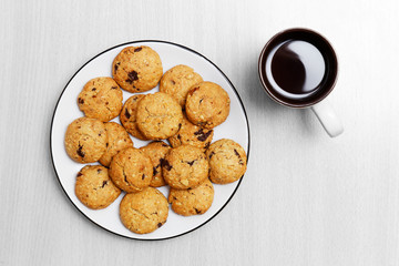 Homemade cookies with nuts and pieces of chocolate and cup of tea on grey wooden table. Top view. Copyspace.