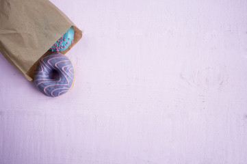 pink and blue donuts in a paper bag, flat lay on purple background.