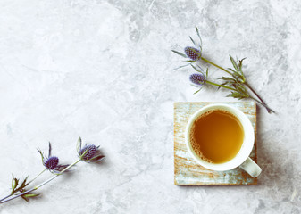 Obraz na płótnie Canvas Cup of Tea and Sea Holly Flowers on gray stone background