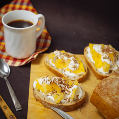 A cup of coffee with pineapple sandwiches, on a black, textured table. Breakfast.