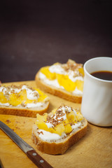 A cup of coffee with pineapple sandwiches, on a black, textured table. Breakfast.
