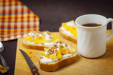 A cup of coffee with pineapple sandwiches, on a black, textured table. Breakfast.