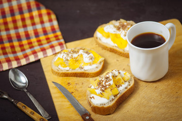 A cup of coffee with pineapple sandwiches, on a black, textured table. Breakfast.