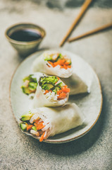 Shrimp and vegetable rice paper spring rolls with sauce on ceramic plate over grey background, selective focus, vertical composition. Asian cuisine, clean eating, vegetarian, dieting food concept
