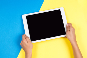 Kid hands with tablet computer on blue and yellow background