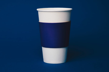 Paper cup for hot drinks, coffe, tea to take away with blue sleeve isolated on blue background
