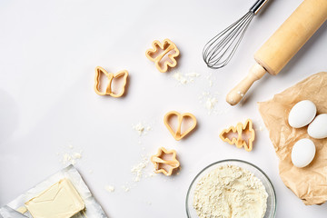 Bowl with wheat flour, rolling pin, whisk, eggs, cookie cutters. Top view on a white table with a copy space