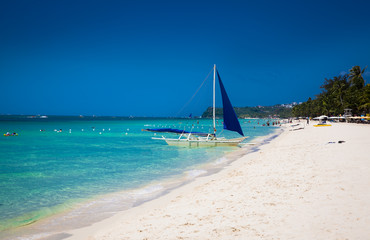 Fototapeta na wymiar Philippine traditional boat with blue sail on White Beach. Boracay, Philippines.