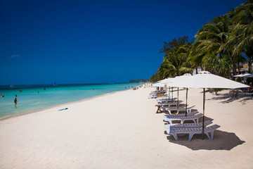 Tropical vacation on white sand beach with sun, blue sky and palm trees. White beach at Boracay, Philippines.