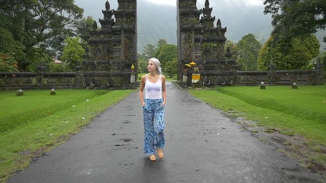 Slow motion shot of woman strolling on a road outside a candi bentar in Indonesia