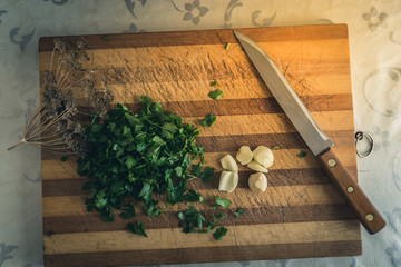 Garlic and parsley on a cutting board, dill and knife, slicing ingredients in the kitchen