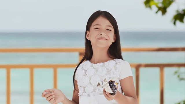Philippine schoolgirl in white dress smiles, eating crispy potato chips. Tropical landscape. The palms. Summer.