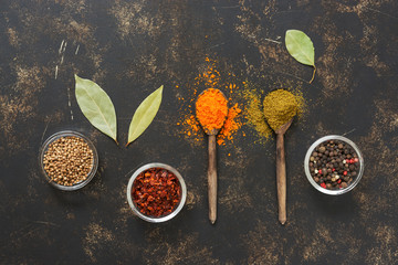 Spices on a dark background with wooden spoons.