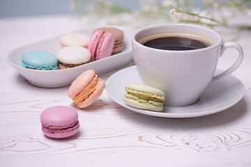 Close-up morning white cup of coffee, cake macaron and flower on blue table. Beautiful breakfast.