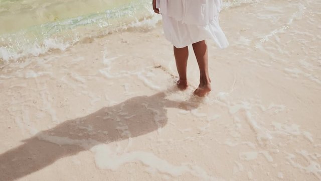 Bare feet of a teenage girl walking along the waves of the tropical coast. White sand. Ocean. Childhood. Happiness.