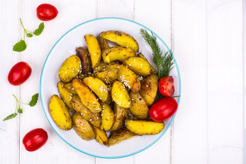 Baked potato slices with herbs and spices on plate on white wooden table