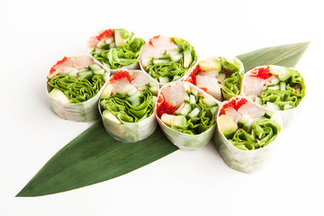 bright spring rolls with fish, caviar and greens a bamboo leaf on a white background