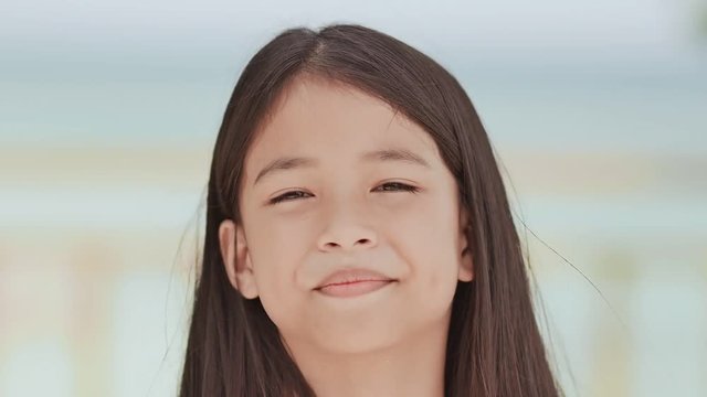 A charming filipino schoolgirl positively poses. Face close-up on a white-blue background of a tropical beach.