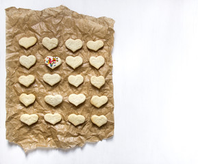 on a white background on the parchment paper for baking lie a cookie in the form of heart on one stump form multi-colored sticks 
